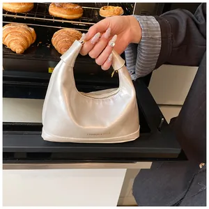 Detail of white glossy dumpling bag with gold lettering held near fresh croissants