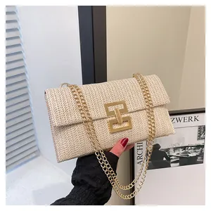 Detail of woven beige straw handbag featuring a large gold buckle and metal chain straps