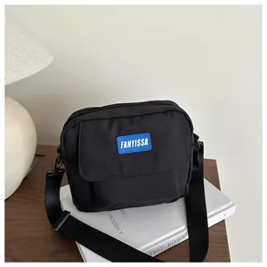 Détail du petit sac bandoulière en toile noire avec patch logo bleu sur bois