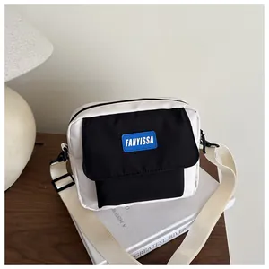 Détail du sac bandoulière carré avec rabat noir contrasté et étiquette tissée bleue