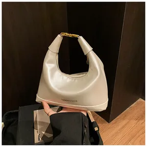 Detail of white half-moon hobo bag with gold hardware and leather texture on wood