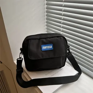 Sac bandoulière noir minimaliste avec étiquette bleue posé sur des livres blancs