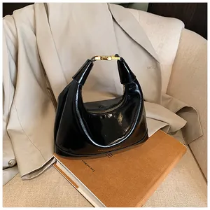 Detail of glossy black hobo bag with golden hardware and fashion logo text on brown book