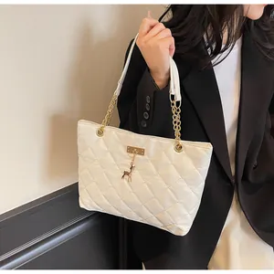 Close-up of white quilted tote bag with gold chain strap and metal deer charm detail