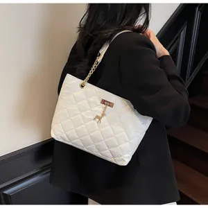Close-up of white quilted tote bag with gold chain strap and deer charm pendant detail