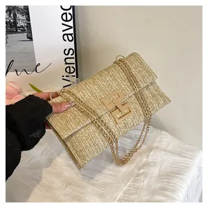 Close-up of straw woven envelope bag with gold geometric lock and metal chain strap