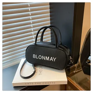 Close-up of black woven baguette bag with BLONMAY embroidery on white decorative books