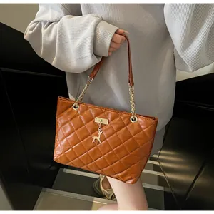 Detail of caramel quilted tote bag with golden reindeer charm and chain strap