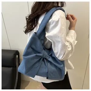 Détail d'un sac à épaule en jean bleu foncé avec un grand nœud porté par le modèle