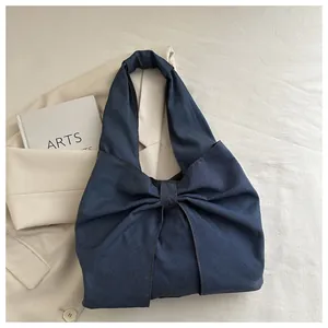 Détail du sac à bandoulière en jean bleu foncé avec un grand nœud et une poignée intégrée