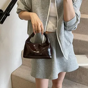 Minimalist dark brown patent leather handbag with glossy finish and shoulder strap