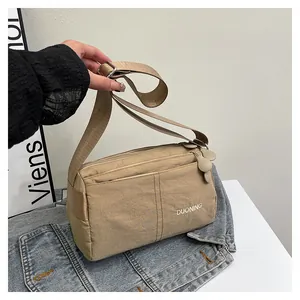Détail du sac bandoulière en nylon kaki avec zips et logo de marque sur du denim