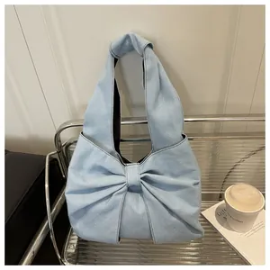 Détail du sac à épaule en jean bleu clair avec grand nœud sur une chaise argentée