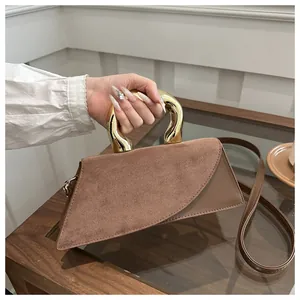 Détail d'un sac en daim marron de forme géométrique avec une poignée en métal doré