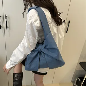 Sac à épaule en jean bleu avec un grand nœud et bandoulière large sur un modèle