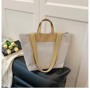Detail of a large canvas tote bag with leather trim and wide shoulder strap in a home setting