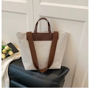 Detail view of large canvas tote bag with brown leather handles and woven shoulder strap