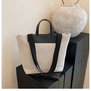 Detail of minimalist canvas tote bag showing contrast leather handles and wide shoulder strap