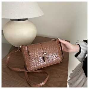 Detailed view of brown woven-textured crossbody bag with gold buckle on wooden table