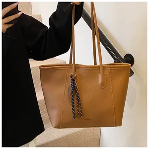 Detail view of caramel brown pebble leather tote bag with stylish woven pendant
