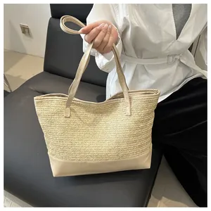 Detail of large woven straw tote bag with khaki leather handles and base, hand-held view