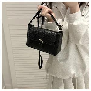 Detail of black woven texture crossbody bag with gold metal buckle on a model
