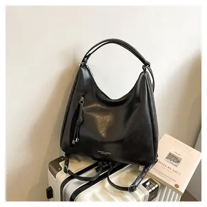 Detail of black faux leather hobo bag with zip pocket and knotted pulls on a suitcase