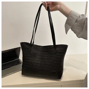 Detail of black woven straw tote bag featuring a durable leather base and smooth shoulder strap