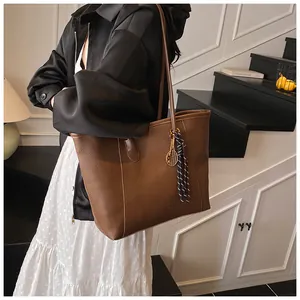 Detail view of large brown leather tote bag with gold tennis racket charm and striped tassel