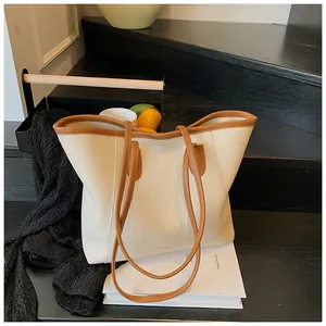 Detail of cream tote bag with brown trim and pebble texture on an indoor staircase