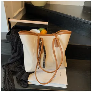 Detail of cream tote bag with brown leather trim and tassel on black wood steps