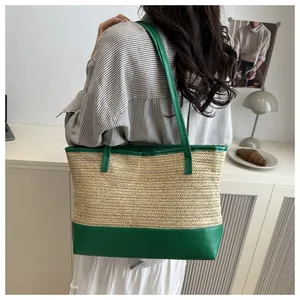 Detail of hand-woven straw tote with green leather handles on a female model