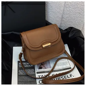 Brown vintage leather shoulder bag with gold cylindrical lock on black silk background