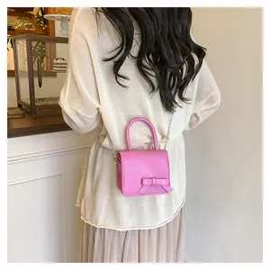 Petit sac carré rose avec nœud et bandoulière chaîne porté par un mannequin