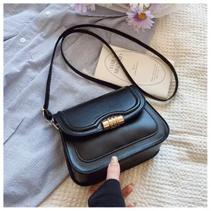 Detail of black leather crossbody bag with a distinctive gold cylindrical metal buckle