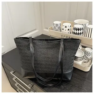 Detail of black woven straw tote bag with smooth leather trim on a modern counter