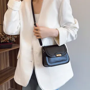 Classic black crossbody flap bag with golden metal buckle on a white blazer model
