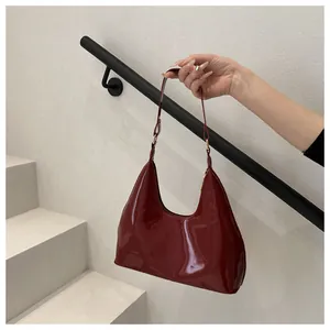 Detail van donkerrode lakslederen hobo-tas met gouden hardware vastgehouden