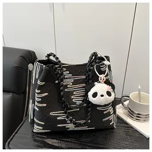 Detail of black tote bag with wave embroidery, chain straps and panda plush charm