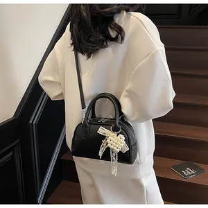 Dettaglio della borsa Boston nera con ciondolo a fiocco in pizzo e perle su modella
