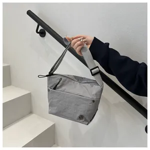 Primer plano del bolso bandolera de nailon gris con logo M de metal y correa ajustable