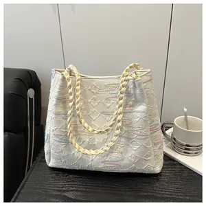 Detail of quilted tote bag with wavy embroidery and woven shoulder straps on wooden surface