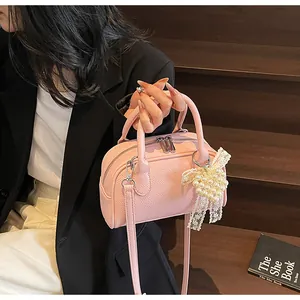 Dettaglio borsa Boston rosa chiaro con ciondolo a fiocco di pizzo e perle su pelle martellata