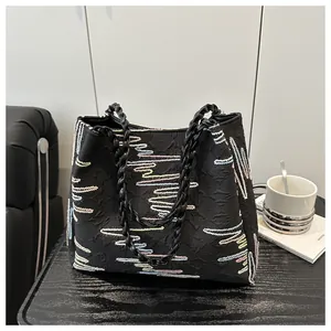 Detail of black tote bag featuring colorful wave embroidery and woven texture strap