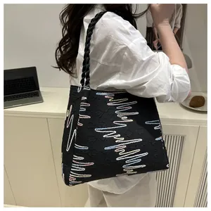 Detail of black tote bag featuring colorful wavy embroidery and woven leather straps