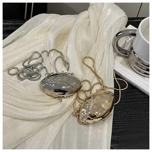 Macro detail of minimalist pebble-shaped gold and silver metal clutch bags with snake chains