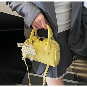 Dettaglio della borsa gialla con fiocco in pizzo e ciondolo di perla su pelle martellata