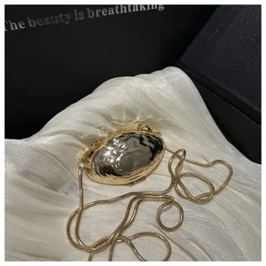 Detailed view of golden metallic shell-shaped evening bag with ripple texture and chain