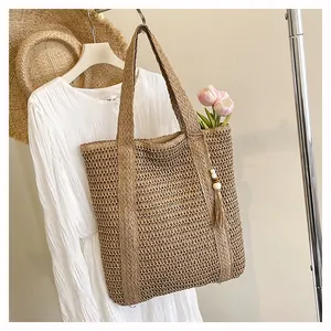 Detail view of woven straw tote bag featuring hollow texture and wooden bead tassel