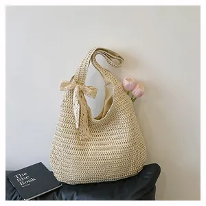Détail du sac à bandoulière en paille beige avec nœud en dentelle et décoration